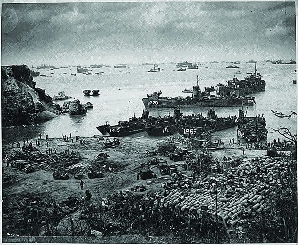 Landing craft and vehicles massed on a beach below a headland